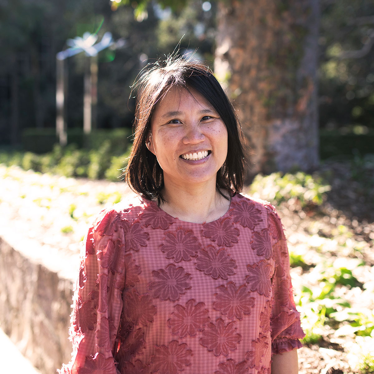 Senior Architect Lai Ho, in pink blouse with flowers, smiling in Roma Street Parkland.