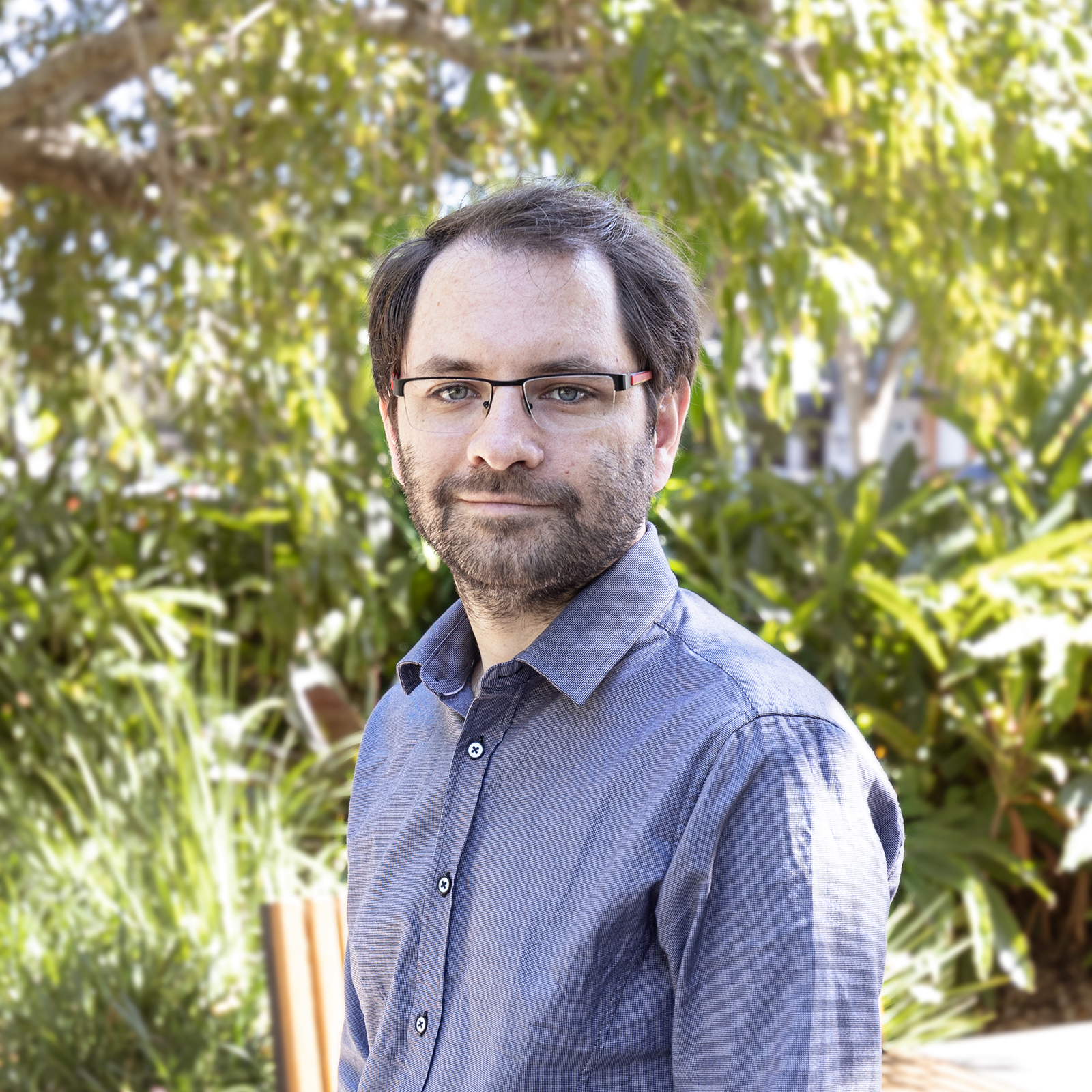 Jacob wearing a blue shirt and standing in front of some greenery at the park.