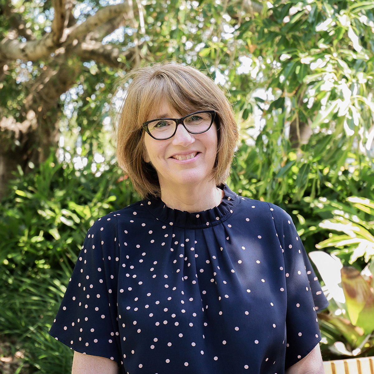 Associate, People and Practice, Faye Holmes smiling in Roma Street Parkland, in a polka dot navy blouse.