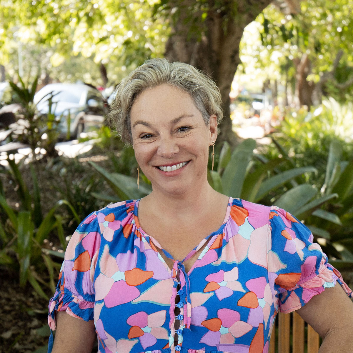 Studio Management, Kyrrin Kedwell smiling in Roma Street Parkland in a colourful blouse.